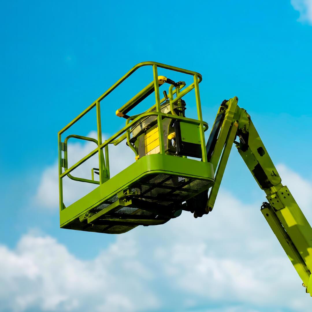 A green aerial lift platform extends against a bright blue sky.