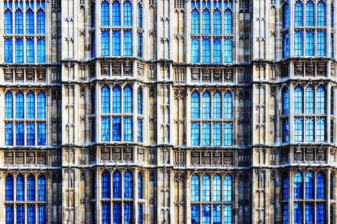 Close-up of a Gothic-style building facade with ornate stonework and numerous blue-tinted windows arranged in a symmetrical pattern.