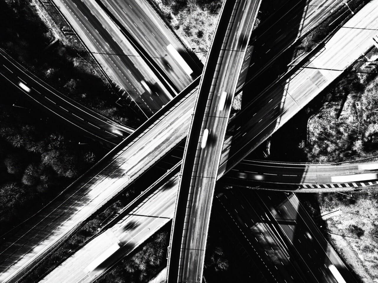 Aerial view of a complex highway interchange with multiple overlapping roads and blurred vehicles, in black and white.
