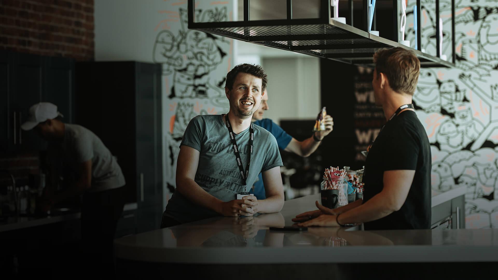 Three people socializing in a modern cafe with graffiti art on the walls; one gives a thumbs-up.