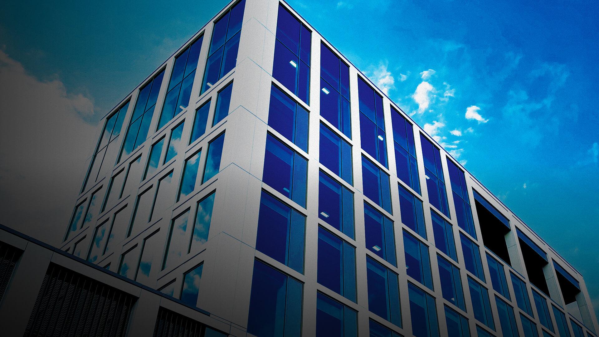 Modern glass building with reflective blue windows against a vibrant blue sky with scattered clouds.