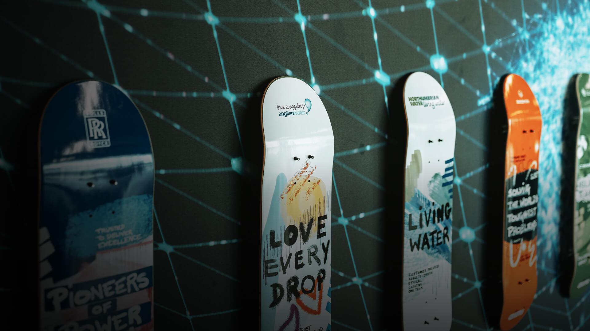 Skateboards with artistic designs and text like "LOVE EVERY DROP" displayed against a digital network-themed background.