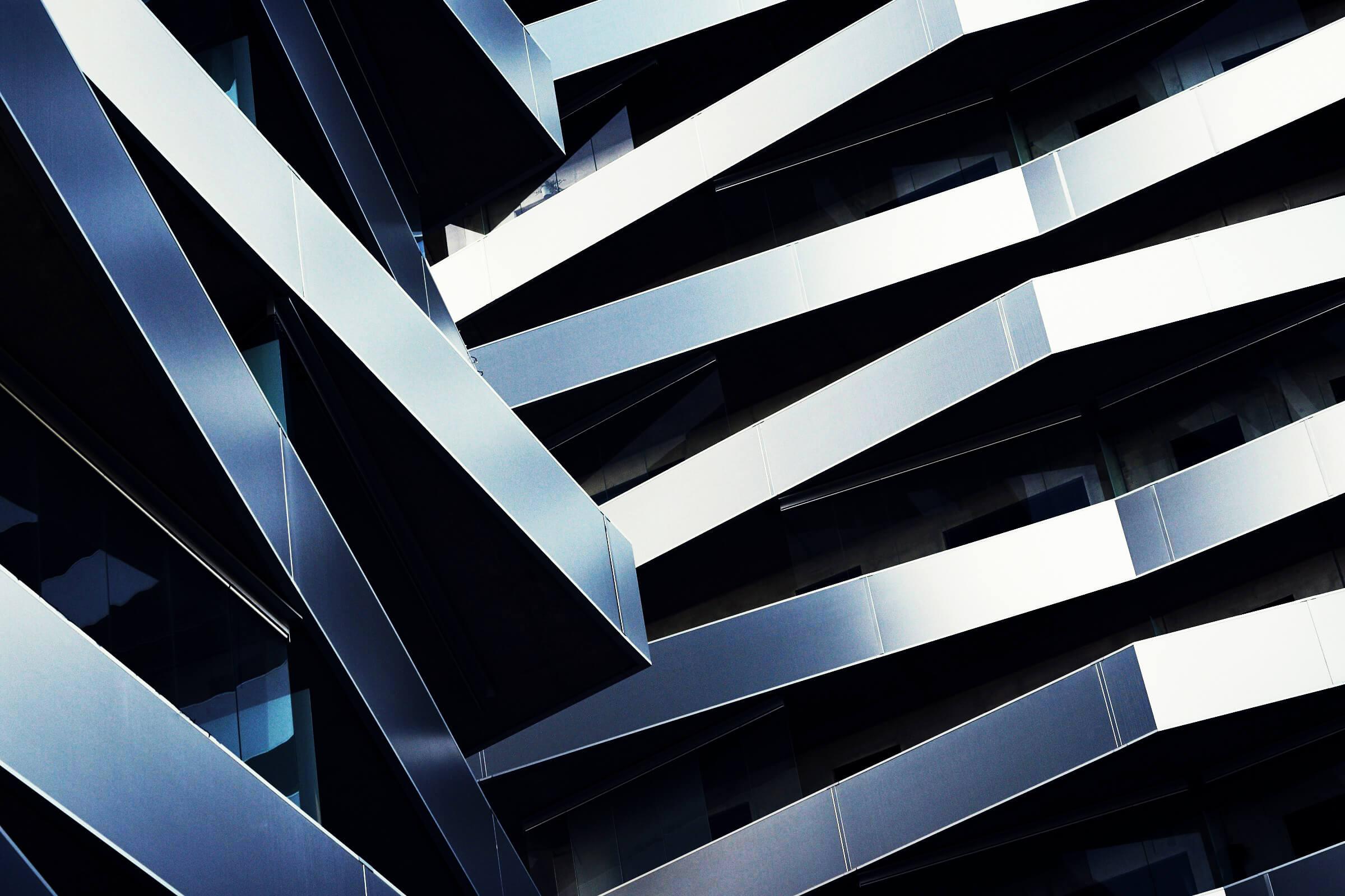Modern building facade with overlapping, angled metal panels creating a dynamic, geometric pattern in shades of blue and gray.