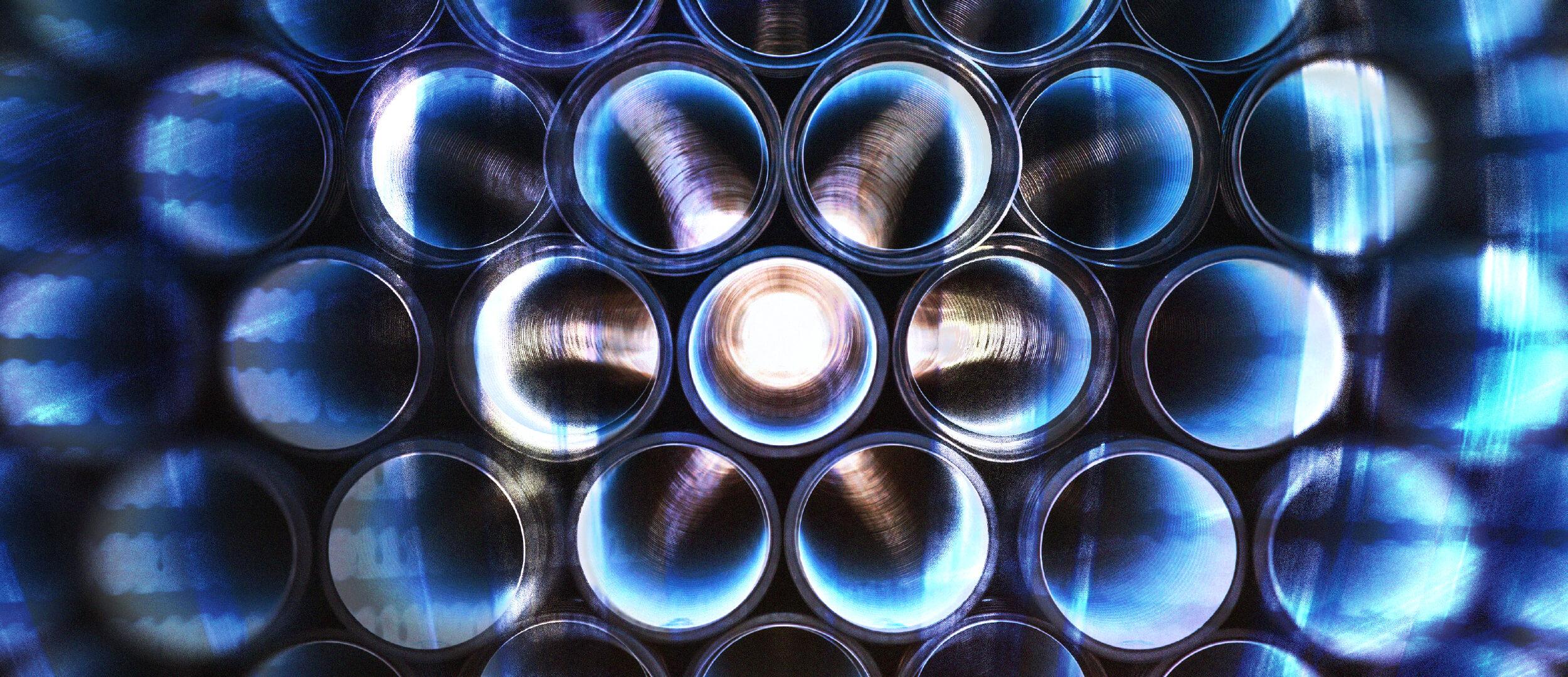 Close-up of reflective, cylindrical metal tubes arranged in a pattern, illuminated with blue and white light, creating a symmetrical design.